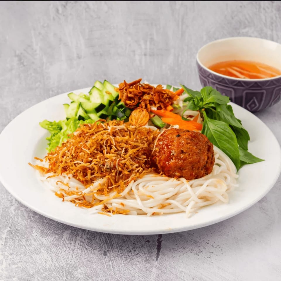 Vietnamese vermicelli noodles with a meatball, crispy fried onions, fresh herbs, and a side of broth.