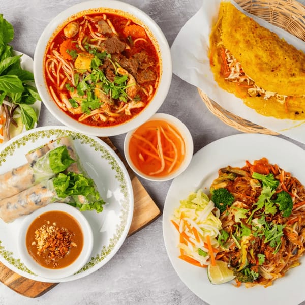 Overhead view of various Vietnamese dishes, including spring rolls, noodle soup, and a savory crepe.