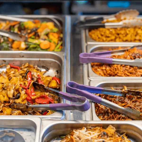 Buffet-style serving trays filled with various colorful Vietnamese dishes, including stir-fried vegetables and noodles.
