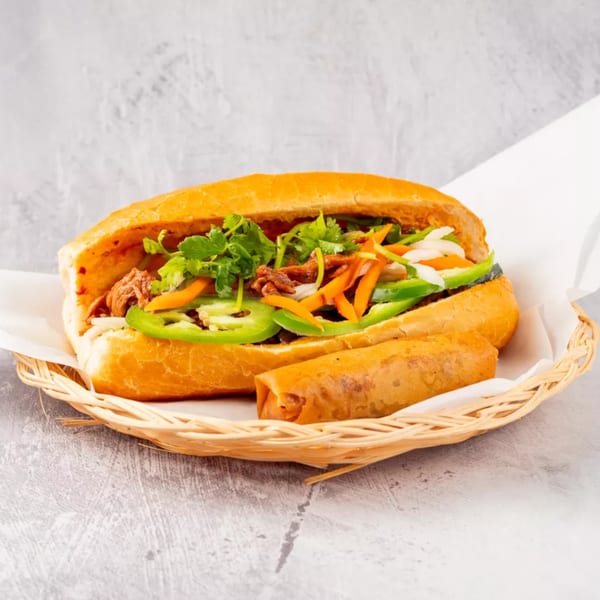 Banh mi sandwich with meat, cilantro, carrots, and peppers, with an egg roll, in a basket.