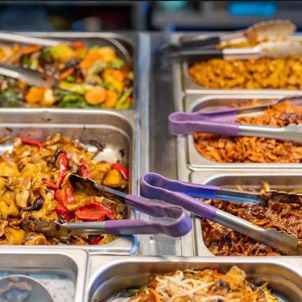 ChuMinh Tofu's buffet line features various Vietnamese dishes in metal trays with serving tongs.