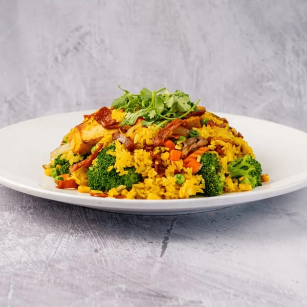 ChuMinh Tofu's vibrant yellow fried rice with broccoli, carrots, peas, corn, and tofu on a white plate.