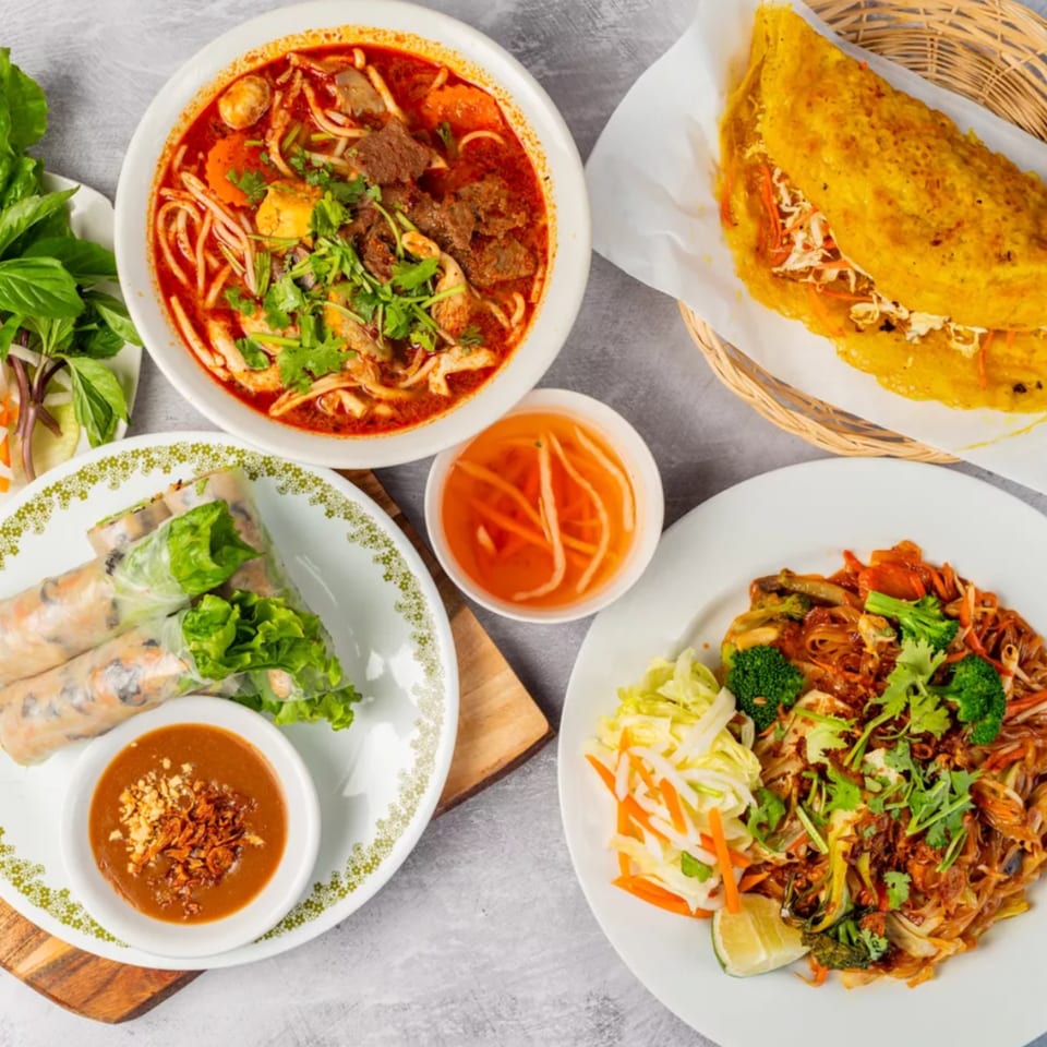 A vibrant spread of Vietnamese dishes, including pho, spring rolls, a savory crepe, and noodles.