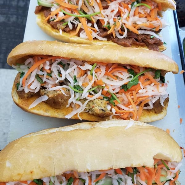 Three ChuMinh Tofu banh mi sandwiches, filled with colorful vegetables and tofu, on a light surface.