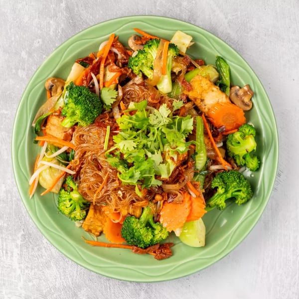 Vietnamese stir-fried glass noodles with tofu, broccoli, carrots, mushrooms, and cilantro on a green plate.